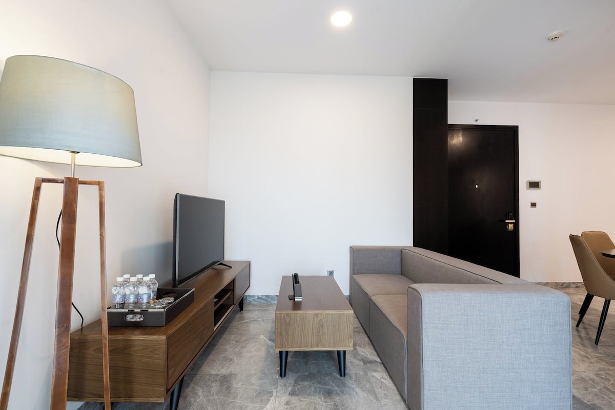 A modern living room with a flat-screen TV, a wooden entertainment unit, a grey sofa, a coffee table, and a floor lamp.