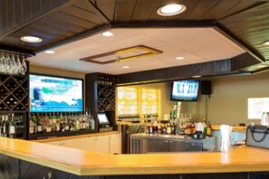 A bar area with a counter, shelves of bottles, and a television screen.