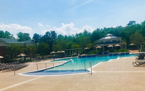 A swimming pool with lounge chairs and umbrellas, surrounded by trees and a building with columns.