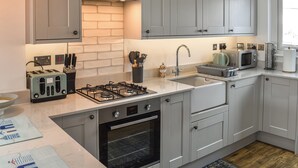 A modern kitchen with grey cabinets, a gas stove, an oven, a sink, and a microwave. - 2 bedroom accommodation in Haverigg (Haverigg)