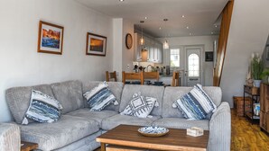A living room with a grey sectional sofa, a wooden coffee table, and a kitchen in the background. - 2 bedroom accommodation in Haverigg (Haverigg)