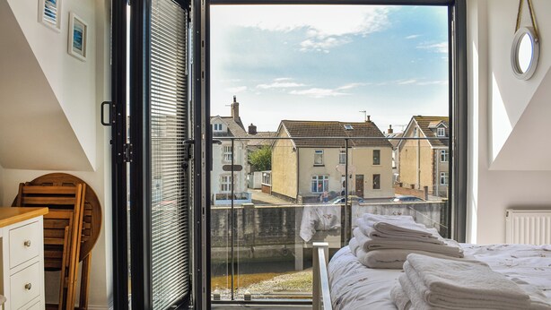 A bedroom with a large window, a bed with neatly folded towels, a wooden chair, and a dresser. - 2 bedroom accommodation in Haverigg (Haverigg)