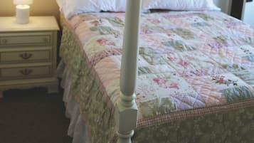 Un llit amb cortines, un col·leccionador de flors, una taula de nit amb una làmpada i un interruptor de llum fixat a la paret.