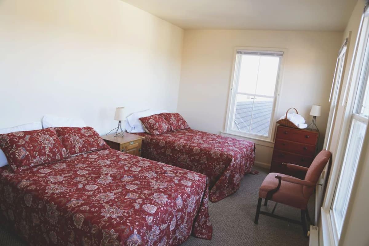 A bedroom with two beds, a dresser, a chair, and a window.