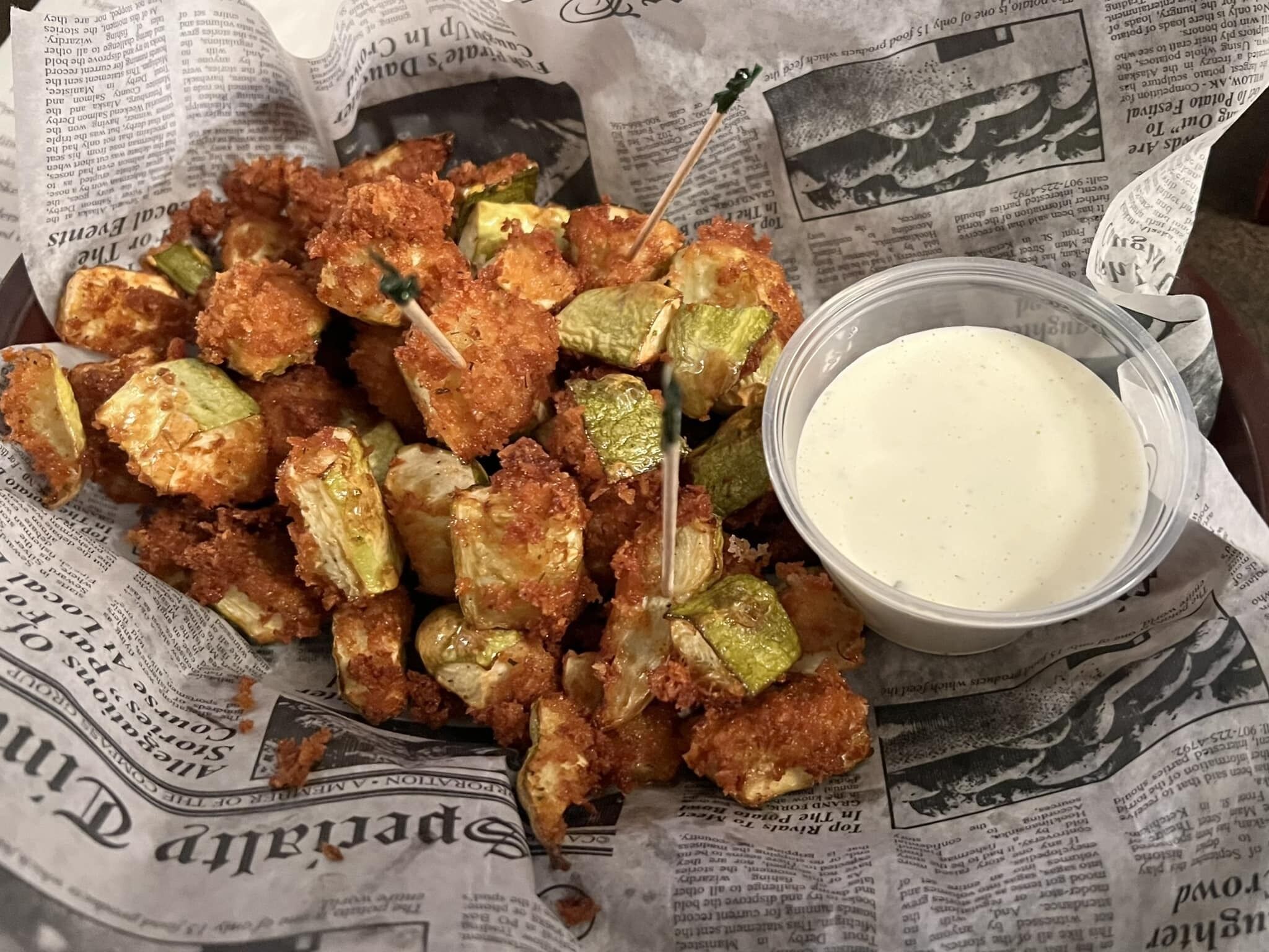 Eine Schüssel mit frittiertem Essen und einer Soße, auf einer mit Zeitung bedeckten Fläche abgestellt.