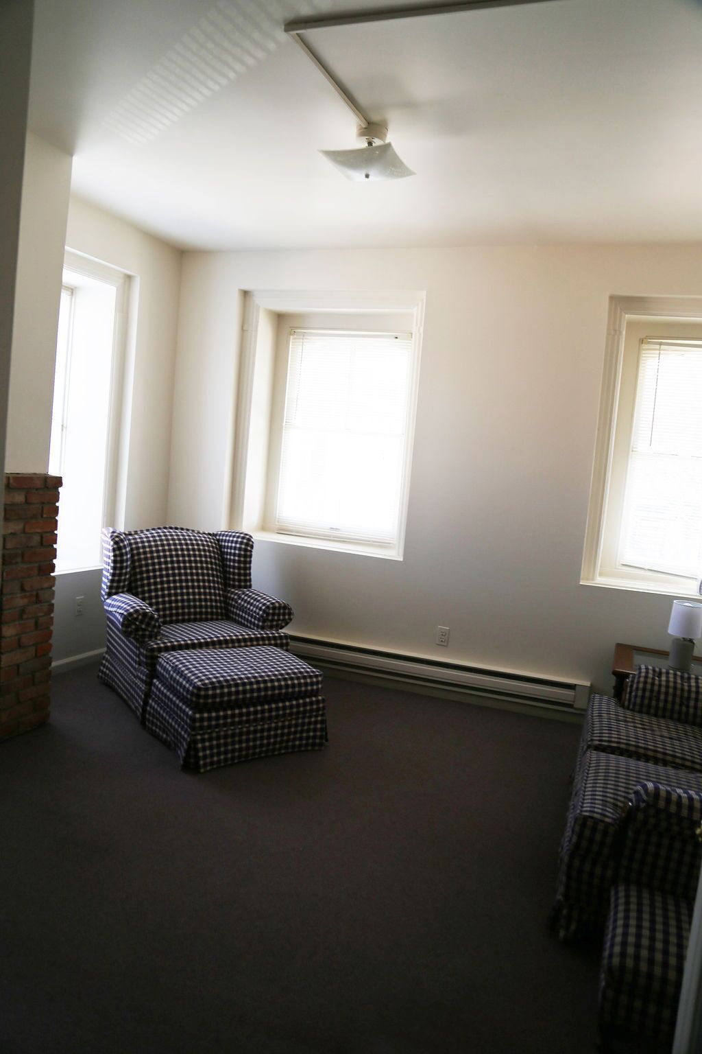 Una habitación con un sillón a cuadros, un reposapiés a juego y una ventana con persianas.