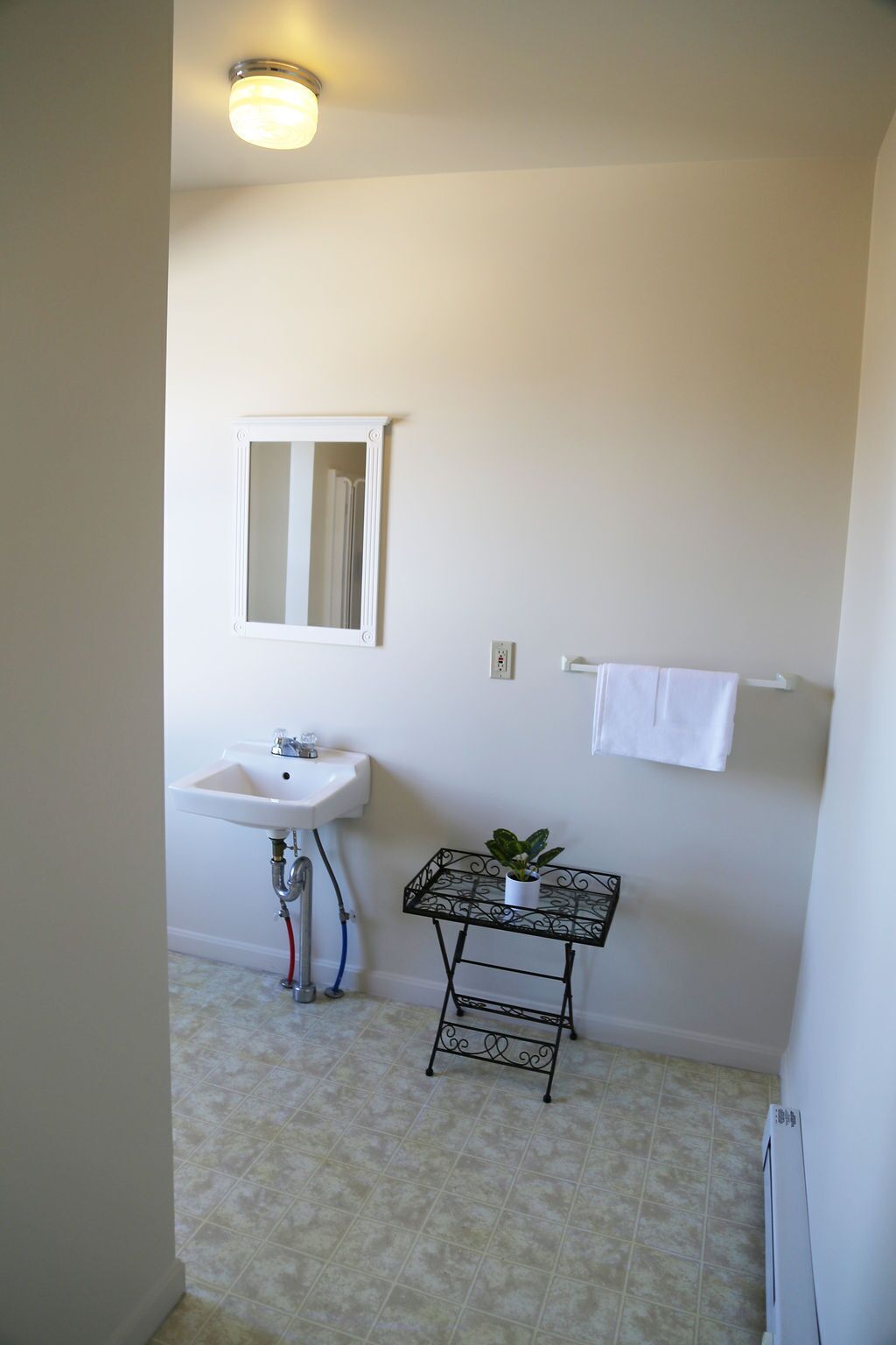 A bathroom with a white sink, a mirror, a small table with a plant, and a towel rack.