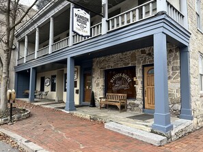 A two-story building with a stone facade and a blue balcony. There is a sign for 'Mansion House Tavern' and a wooden bench outside. - Stoner's Mansion House (Mercersburg)