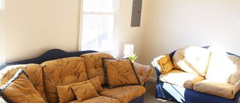 A living room with two sofas, a small ottoman, and a window with blinds.