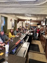 Zona de bar con una barra alargada, taburetes y una variedad de botellas y vasos.