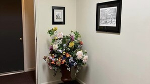 Un pasillo con una puerta de madera, un arreglo floral en maceta y dos cuadros en la pared.