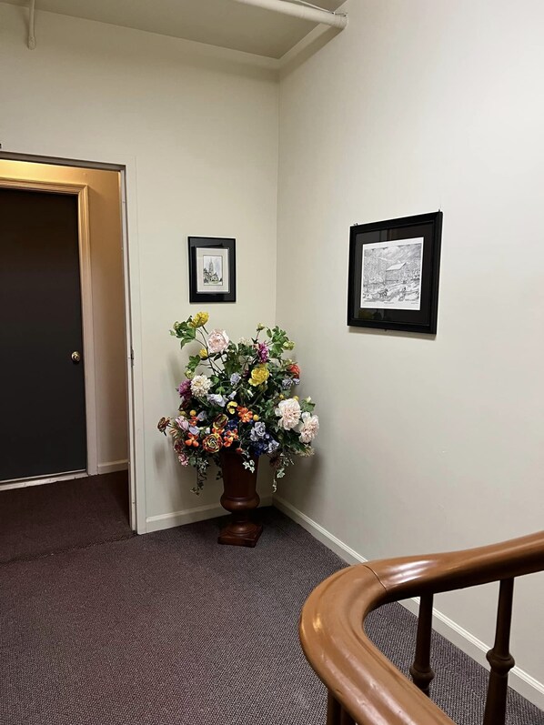 A hallway with a wooden door, a potted floral arrangement, and two framed pictures on the wall. - Stoner's Mansion House (Mercersburg)