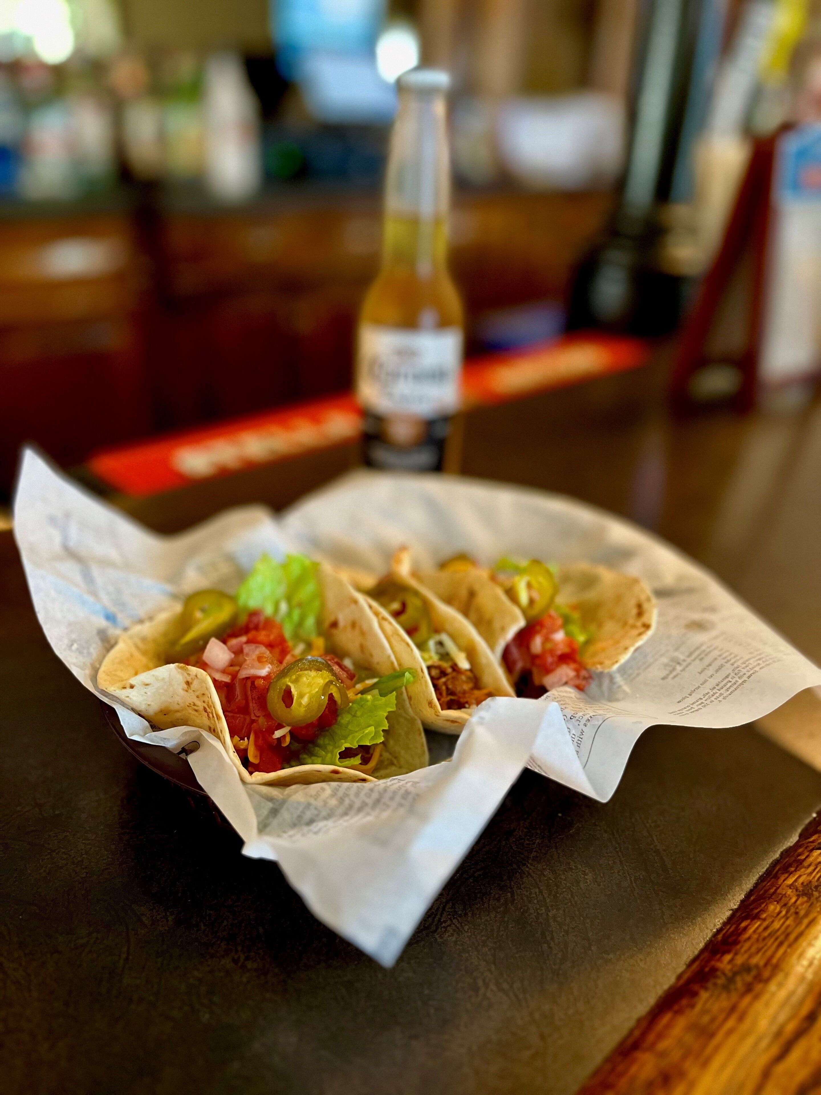 Une assiette de tacos avec une bouteille de bière en arrière-plan.