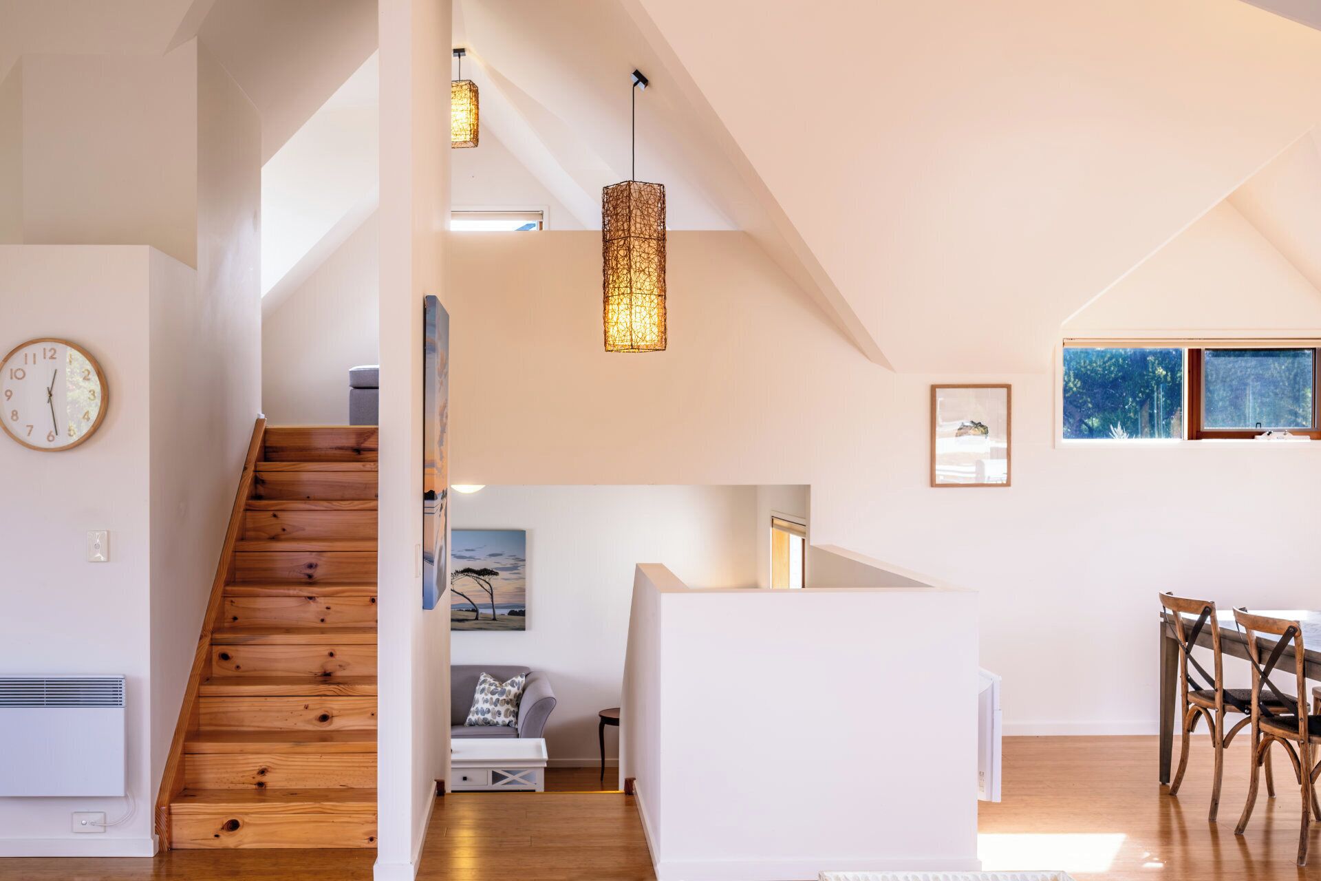 Un intérieur spacieux avec un escalier en bois, un coin repas avec des chaises en bois et une grande fenêtre qui laisse entrer la lumière naturelle.
