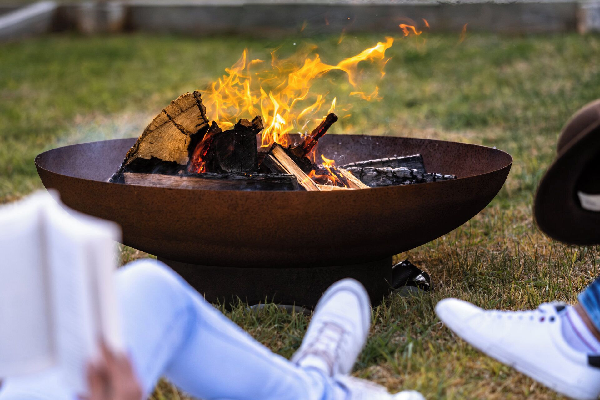 Ein Lagerfeuer mit brennenden Holzscheiten und Flammen, umgeben von Gras.