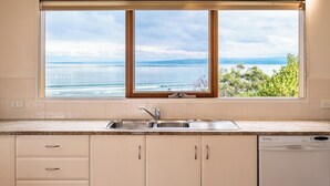 A kitchen with a large window offering a view of the sea and mountains. - Hamptons Hideaway - Freycinet Holiday Houses (Coles Bay)