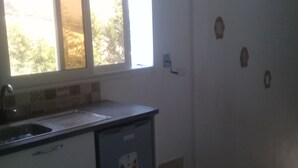 Eine Küche mit Spüle, kleinem Kühlschrank und einem Fenster mit Jalousien.