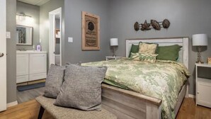 Un dormitorio con cama, mesitas de noche, un banco, un espejo y un adorno en la pared.