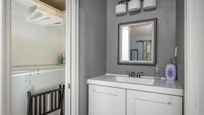 Un baño con un lavamanos blanco, un espejo y un perchero para toallas.
