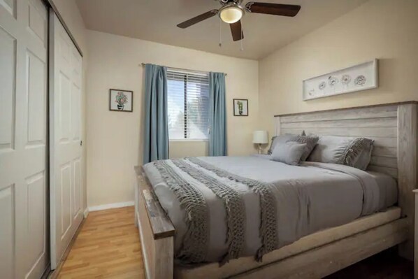 Un dormitorio con cama, ventilador de techo, ventana con cortinas y una obra de arte colgada en la pared.