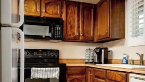 Una cocina compacta con armarios de madera, un microondas, un horno y una cafetera.