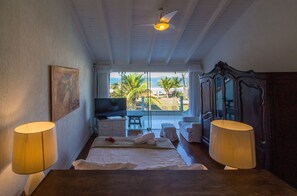 A hotel room with a bed, two lamps, a television, and a view of the beach. - Greenville (Búzios)