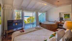 A hotel room with a large bed, a television, a bathtub, and a view of the outdoors. - Greenville (Búzios)
