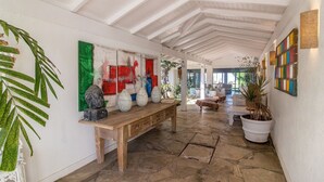 A hallway with a wooden bench, a large abstract painting, and a potted plant. - Greenville (Búzios)