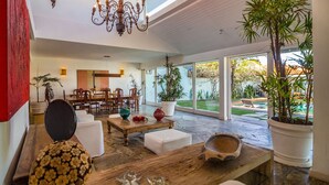 A spacious living area with a high ceiling, a chandelier, and a dining area with wooden furniture. - Greenville (Búzios)