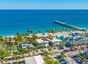 A coastal area with a beach, palm trees, a pier, and a parking lot. - Dan's by the Sea (Lauderdale-by-the-Sea)