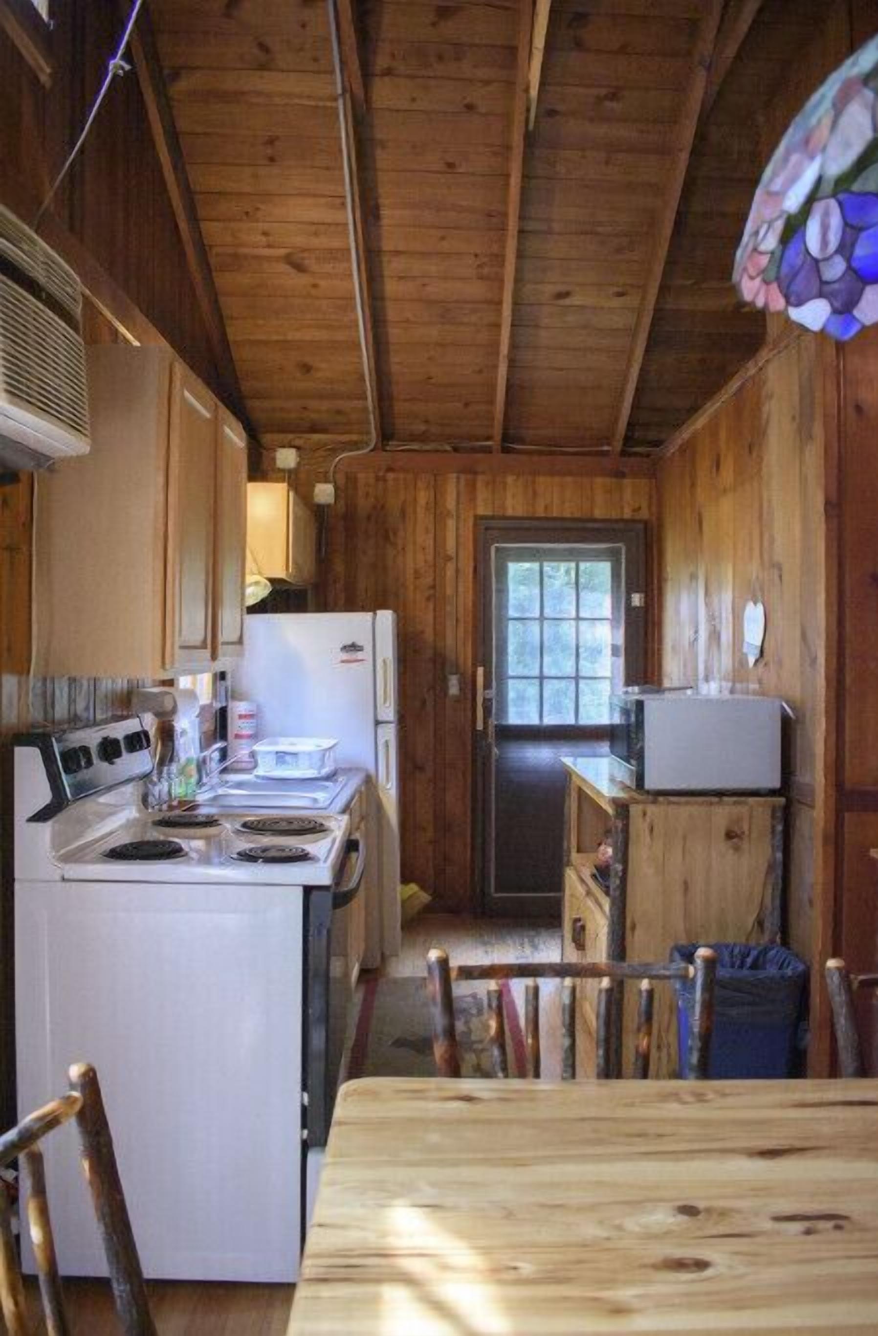 Una cocina compacta con paredes de madera, estufa, refrigerador y microondas.