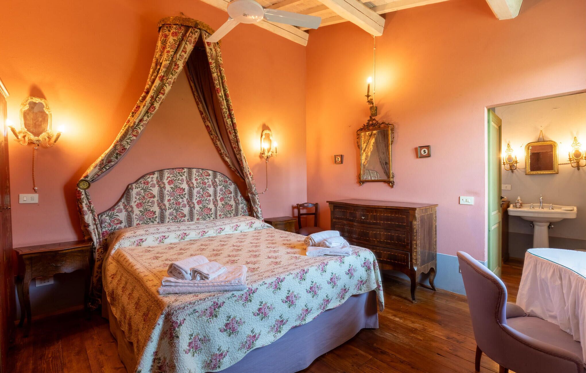 A bedroom with a four-poster bed, a dresser, a vanity with a mirror, and a chair.