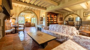 A spacious living room with a high ceiling, exposed wooden beams, a fireplace, a large bookcase, and a comfortable sofa. - Amazing home in Città della Pieve (Città della Pieve)
