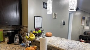 Une cuisine dotée de plans de travail en granit, d’une machine à café, d’un panier de fruits, d’un bol de chips et d’un certificat encadré accroché au mur.