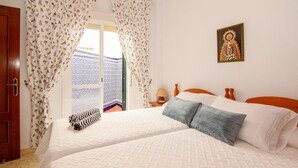 Une chambre à coucher avec un lit, des rideaux, une table de chevet, une lampe et un tableau encadré accroché au mur.