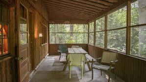 Une terrasse couverte avec des murs en bois, de grandes fenêtres et une table entourée de chaises.
