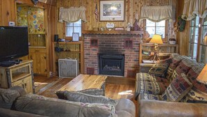 Une chambre confortable, aménagée dans le style d’un chalet, avec une cheminée, des murs en bois, un canapé et un téléviseur.