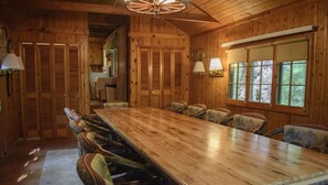 Une salle à manger en bois, avec une longue table et des chaises, des murs en bois et des fenêtres.