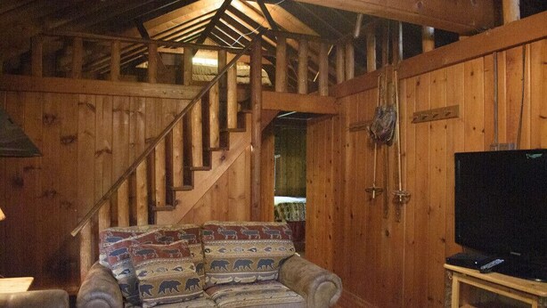 L'intérieur d'un chalet en bois, avec un canapé, un escalier et un téléviseur.