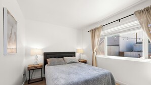 A bedroom with a bed, two bedside tables, a window with curtains, and a view of the outside. - Updated and Cozy Apartment in heart of OB!  (San Diego)