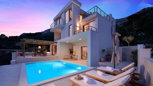 A modern two-story house with a swimming pool, outdoor seating, and a mountain backdrop.