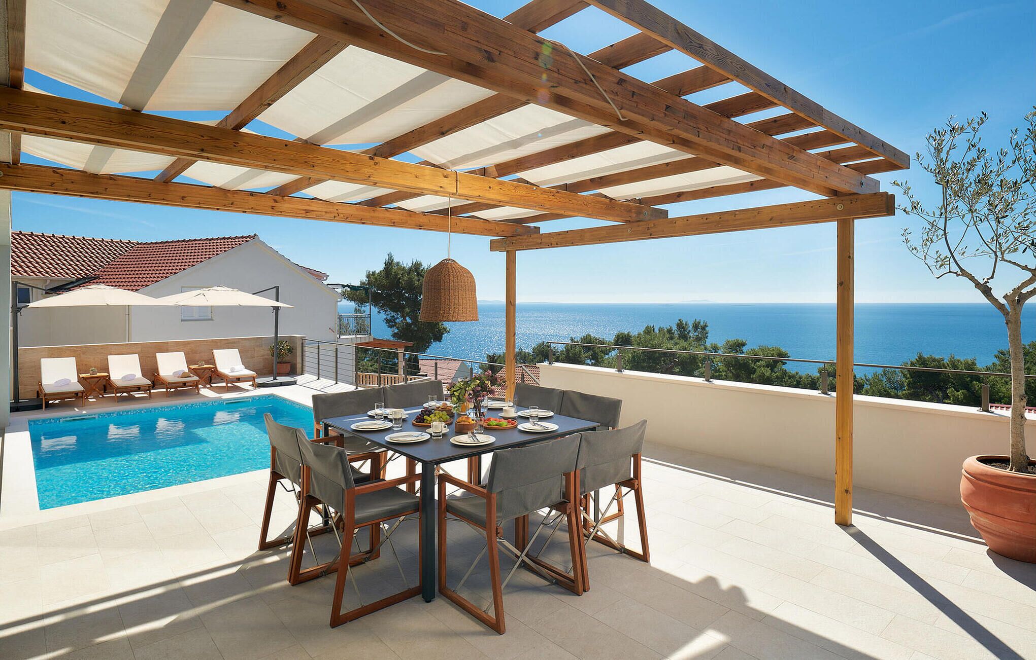 A poolside area with a table set for dining, overlooking a clear blue sea.