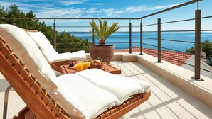 A balcony with two wicker lounge chairs, a large potted plant, and a tray with fruits and glasses of orange juice.