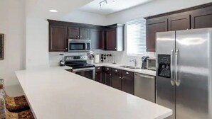 A modern kitchen with dark cabinets, stainless steel appliances, and a white countertop. - In the middle of the Action (Phoenix)