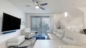 A modern living room with a flat-screen TV, white sofas, a coffee table, and a ceiling fan. - In the middle of the Action (Phoenix)