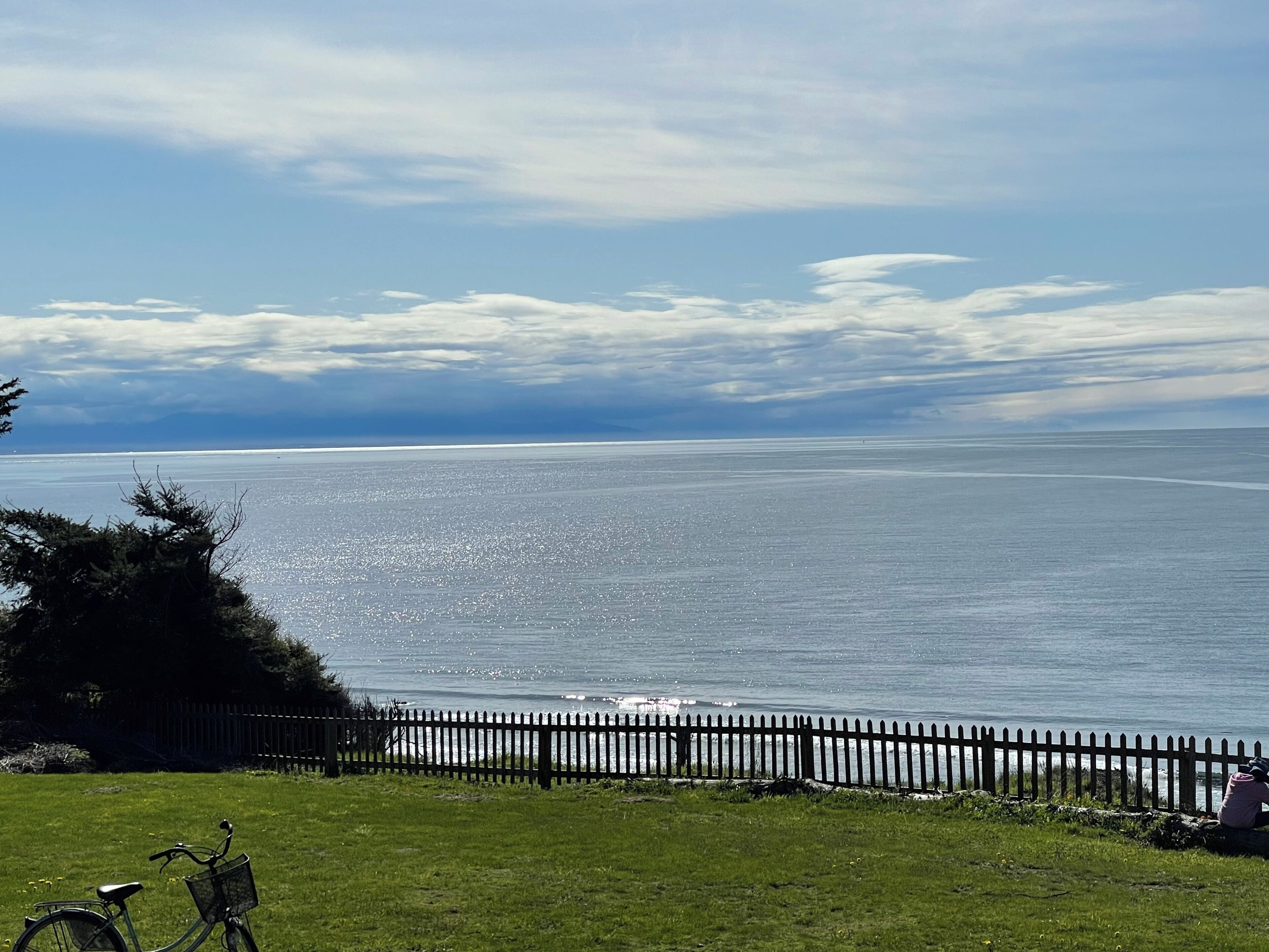 A coastal view with a wooden fence, a bicycle, and a grassy area.