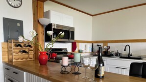 A kitchen with a wooden countertop, a red vase with flowers, a wine bottle, and two wine glasses. - Home Away From Home… for you and for your pets! (Oak Harbor)