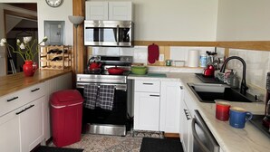 A modern kitchen with white cabinets, stainless steel appliances, and a red trash bin. - Home Away From Home… for you and for your pets! (Oak Harbor)