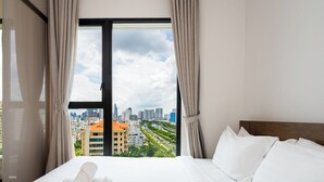 A hotel room with a large bed, white linens, and a view of a cityscape through a large window. - D1 Mension Building (Ho Chi Minh City)