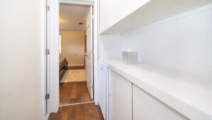 A narrow hallway with white walls and a wooden floor leading to a room with a bed and a door. - Comfort Living Near LRMC, Medical Row
 (Lakeland)
